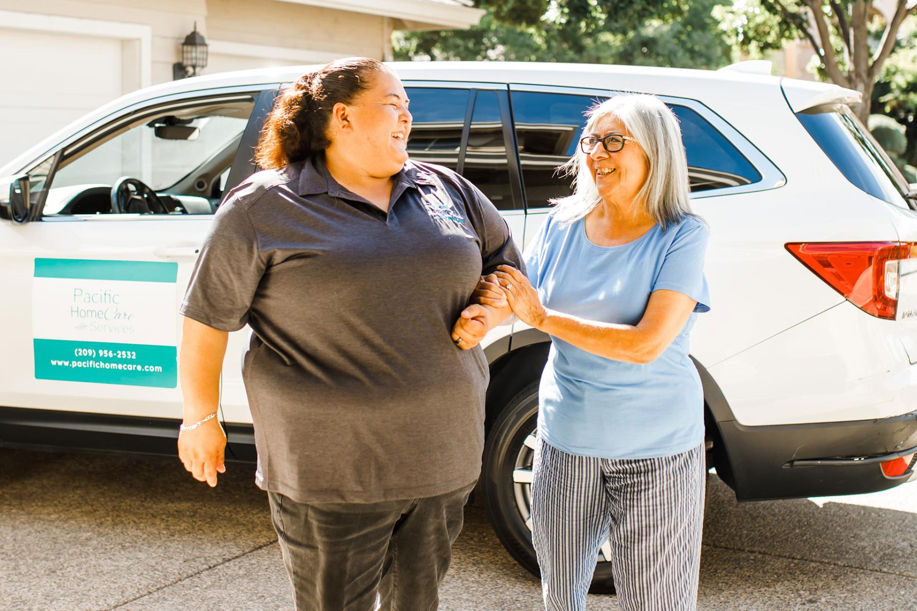 Female care provider assisting elderly female client into home from car