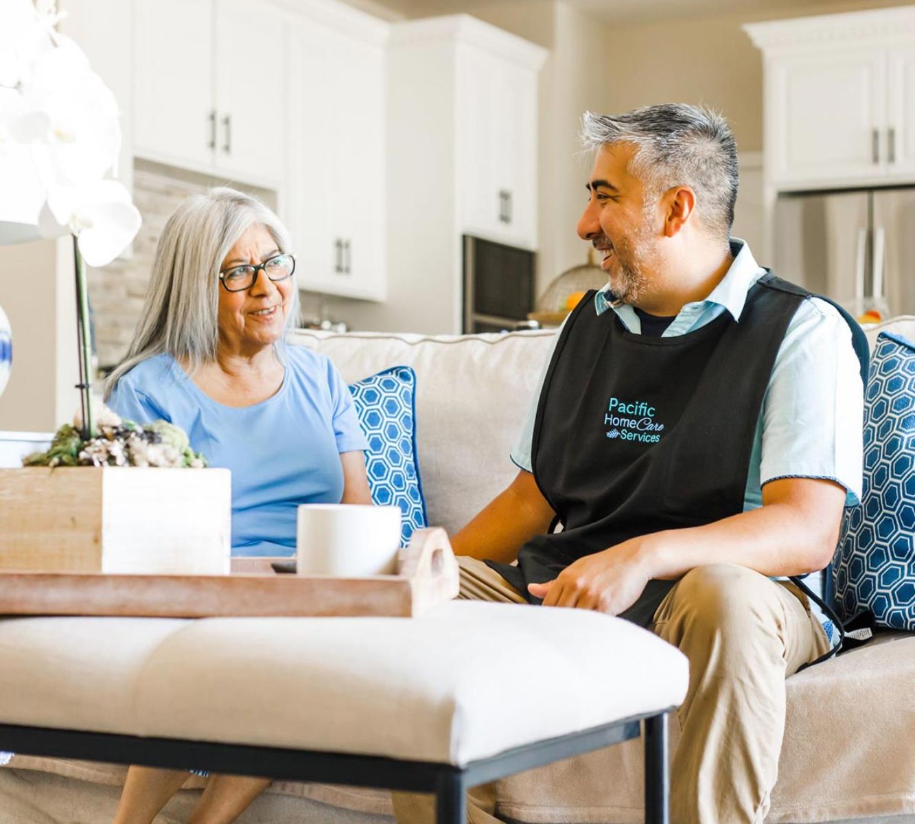 Male care provider conversing with elderly female client on the couch