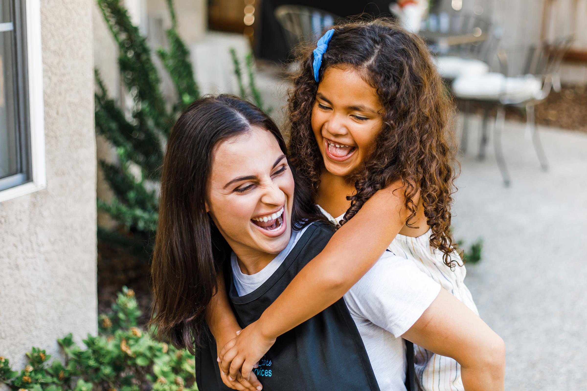 Female care provider giving piggy back ride to female child