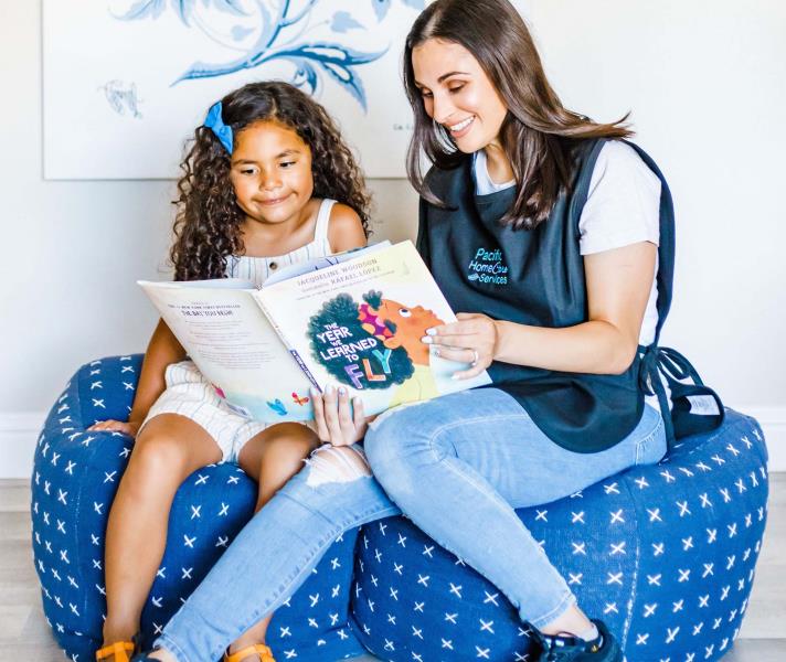 Female care provider reading a book to a female child